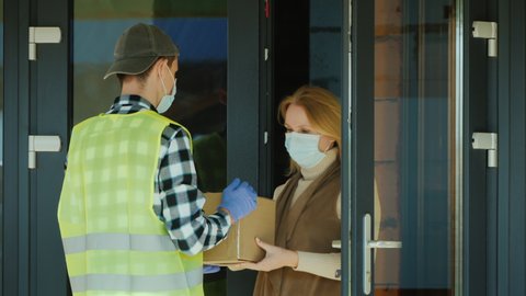 A courier wearing a mask and protective gloves delivers a parcel. Working in a pandemic