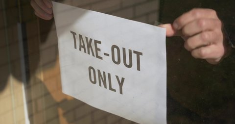 A cafe owner puts a TAKE OUT ONLY sign on the front door. Take out or carry away quickly became the only option for restaurants and bars during the coronavirus COVID-19 pandemic of 2020.  	
