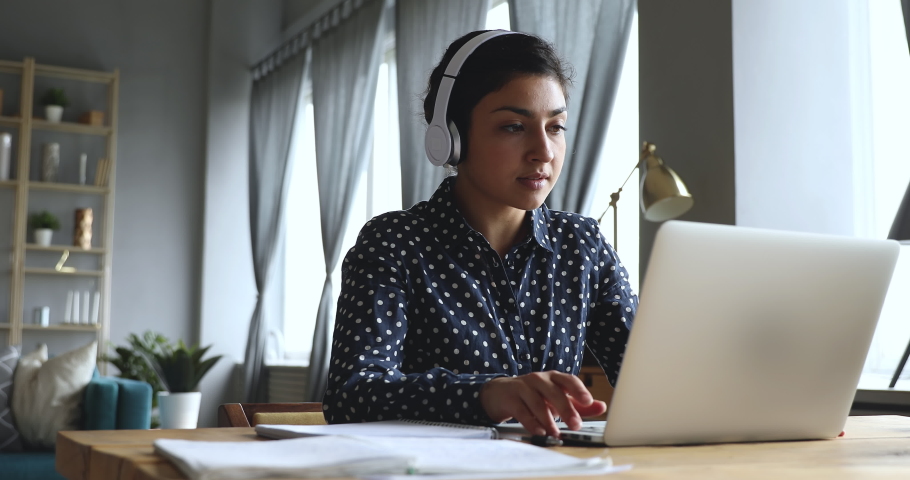 Focused young indian student wearing wireless headphones, studying on online courses, using paper notes. Motivated millennial hindu internet teacher giving language class by conference video call. Royalty-Free Stock Footage #1048820521