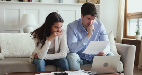 Frustrated young adult couple feeling stressed about high mortgage rates doing paperwork at home. Angry husband and wife renters calculating household payments, having financial problems or bank debt.