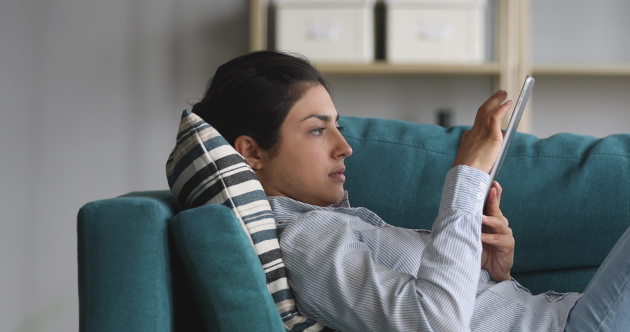 Side view happy young indian woman lying on cozy sofa, studying design apps on digital computer tablet. Motivated millennial hindu designer drawing sketches, smiling girl editing photos alone at home. Royalty-Free Stock Footage #1048820572