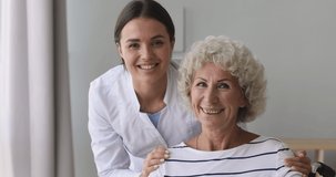 Head shot smiling young medical worker embracing shoulders of happy 70s retired female pensioner, posing for photo. Video portrait of pleasant older woman and doctor nurse volunteer looking at camera.