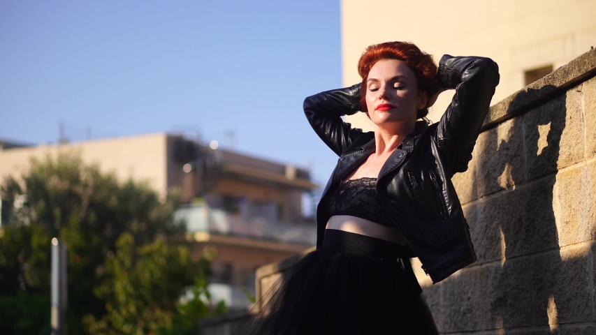 A beautiful red-haired woman in a black leather jacket stretches and puts on her glasses