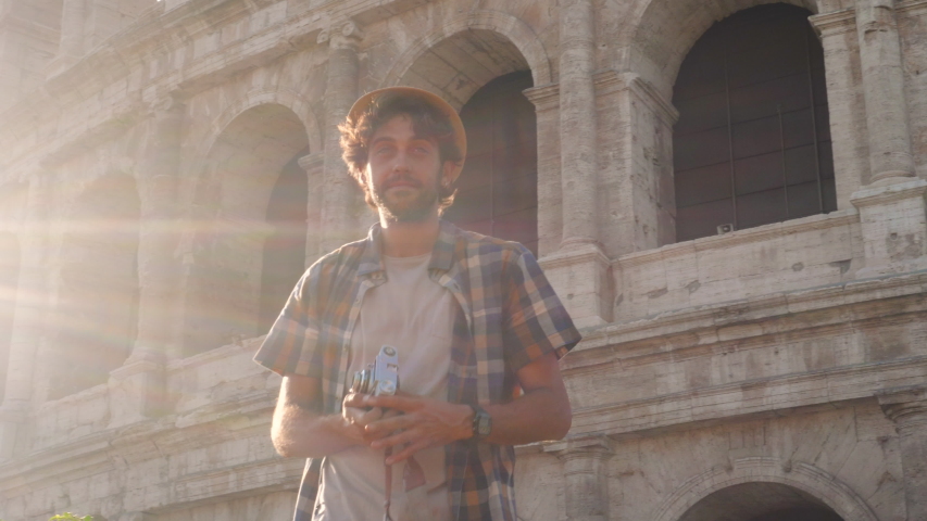 Happy young man tourist with bike wearing shirt tanding on a column taking funny pictures and selfies at colosseum in Rome, Italy at sunrise.