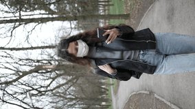 Young woman in medical mask on her face walking in forest and learning news about epidemic in mobile phone. Adult female covered her face with mask to protect yourself from diseases. vertical videos.