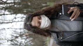 Young woman in medical mask on her face walking in city and learning news about epidemic in mobile phone. Adult female covered her face with mask to protect yourself from diseases. vertical videos.