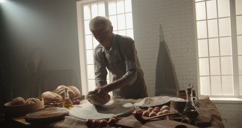 Professional senior moustached caucasian baker working in bakery shop in morning, kneading dough for bread, using traditional recipes, elderly man enjoying his hobby after retiring 4k footage