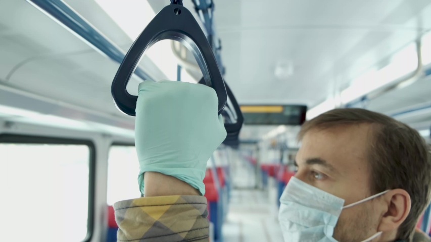 Disease outbreak, stop coronavirus covid-19 pandemic, protect yourself from virus. Adult man with medical protective inside empty train or metro. Focus on hand in protective glove holding handle.