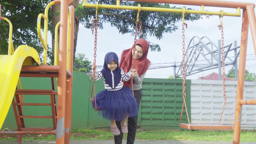 Happy Muslim little girl playing on the swing with her mother at the park. Shot in 4k resolution
