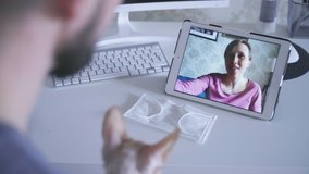 Young man and woman are having video call during viral quarantine at home spbas. American people talking in online chat with smiles, using tablet at table in light room. Couple in relationship is