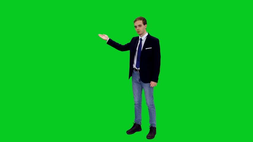 Young stylish business man in suit jacket standing and presenting something on green screen background, Chroma key 4k footage
