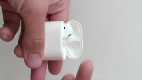 Izmir, Turkey - July 11, 2019: Vertical version footage of Apple Brand airpods 2 opening the charging case and taking the airpods inside by two male hands.