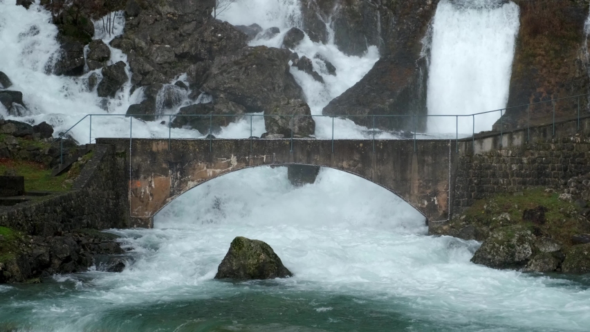 Hillside gushing waterfalls flowing under arched bridge