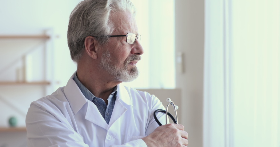 Confident thoughtful senior adult male professional medic, old doctor wears white medical coat glasses holding stethoscope looking through window dreaming, thinking or healthcare and medicine concept. | Shutterstock HD Video #1048870717