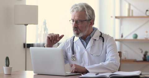 Older doctor talking to patient making video call on laptop. Senior male physician speaking looking at pc screen communicating by webcam in web chat consulting client online. Telemedicine concept