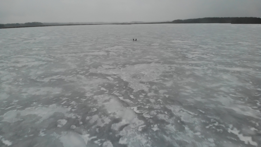 aerial view Two fisherman on the frozen lake at winter fishing in the forest.