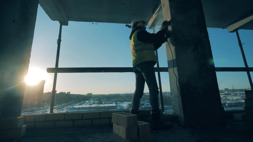 Male constructor is polishing a column at the building site