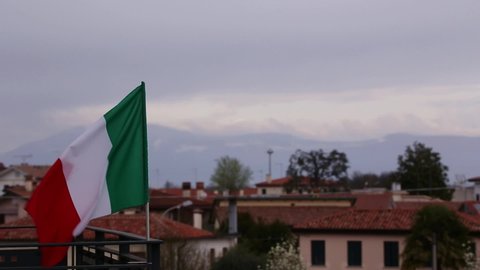 Italian flag waving on the wind on a balcony with a city in