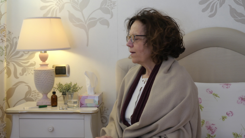 Portrait of ill woman at home. Sick middle aged woman taking temperature at home. Medical problems and fever concept, shot in 4K