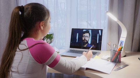 Schoolgirl video chatting with a teacher at home during the coronavirus epidemic in the city. Distance education concept, on-line education at home.