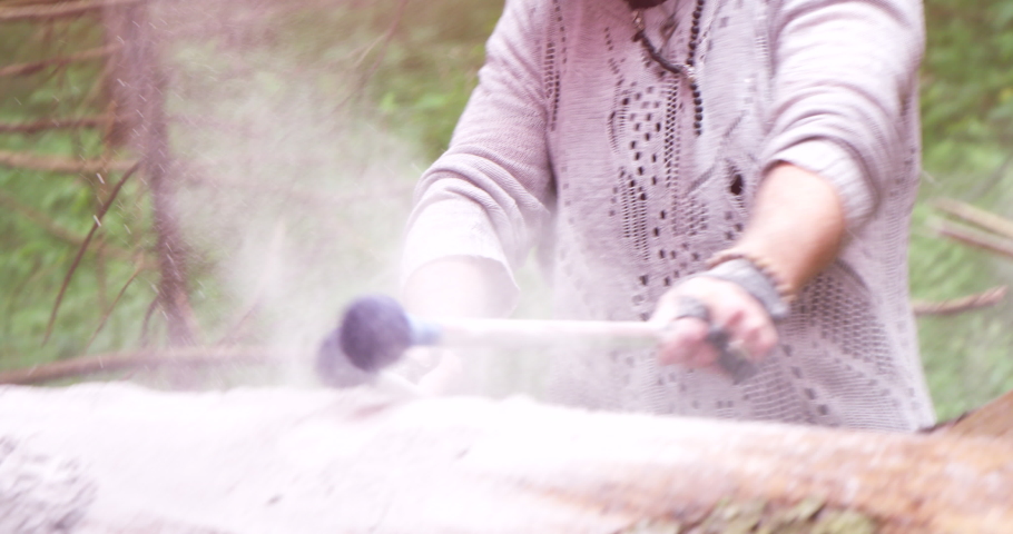 Artistic slow-motion closeup of drumsticks hitting dusty tree trunk in the woods
