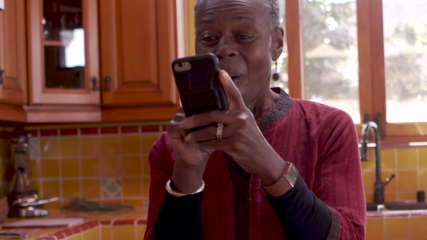 Happy older African American black woman using her mobile phone dancing and smiling while checking her messages or browsing online Royalty-Free Stock Footage #1048900879