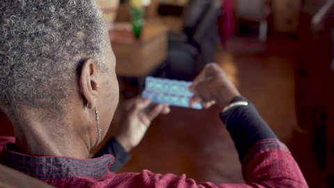 Older black woman closing her daily pill dispenser after filling it with her prescription medicine as a reminder to remember to take her drugs - rack focus from person to organizer