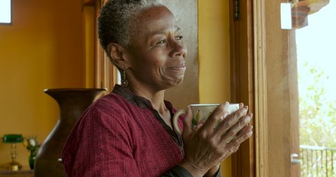 Portrait of a beautiful African American senior black woman in her 60s holding a hot coffee or tea cup, smiling, and looking at camera