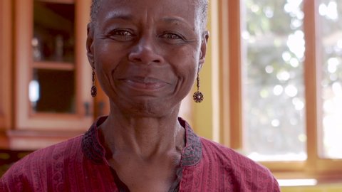 Smiling happy mature senior African American black woman in her home pointing at the camera rack focus from her face to the tip of her finger