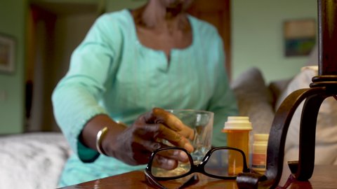 Happy, smiling, attractive senior black woman taking her prescription medication from her daily pill organizer and then putting on her glasses to look out a window
