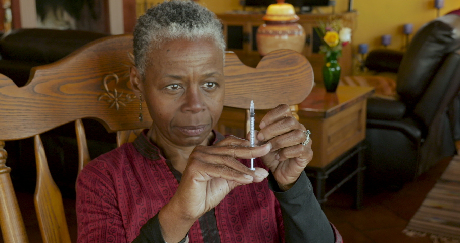 Elderly black woman giving herself an insulin injection with a needle and syringe for treatment of her diabetes illness - medium shot Royalty-Free Stock Footage #1048902127