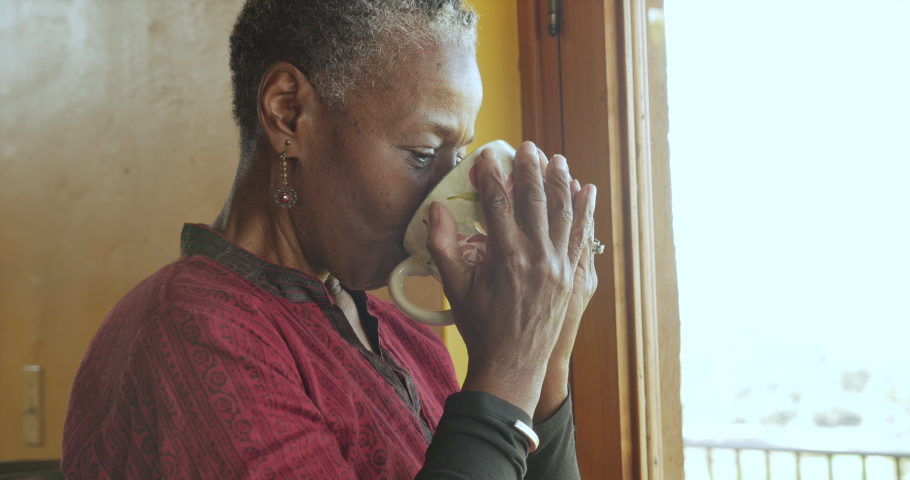 Close up portrait of an attractive African American black senior woman smiling and holding a coffee cup while standing in front of a window Royalty-Free Stock Footage #1048902160