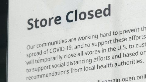 Close up rack focus on notice at store front stating closure from the COVID-19 virus during lockdown.