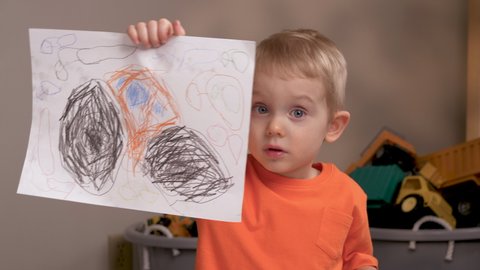 The child in orange tshirt is showing his picture drawn by colored pencils. Children's art and crafts,education, learning activities for kids concept. 
