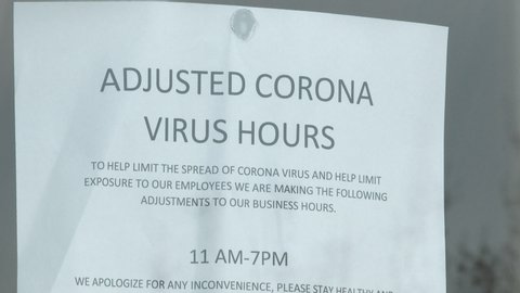 People walk through door with sign reading "Adjusted Corona Virus Hours" during the lockdown from COVID-19 pandemic.