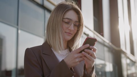 Rotation close up view of young attractive woman in glasses stay near business building smile using phone