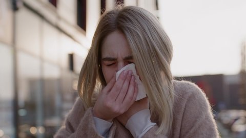Young caucasian woman stand sneezing coughs feel sick fever flu coronavirus symptoms cold allergy city beautiful disease female nose lady runny tissue air pollution adult illness district slow motion