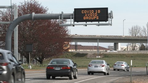 Highway sign reads "COVID 19 AVOID GROUPS" over roadway with vehicles speeding by in Portland, Oregon.