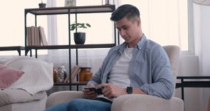 Domestic leisure. Young man watching funny videos on cellphone at home