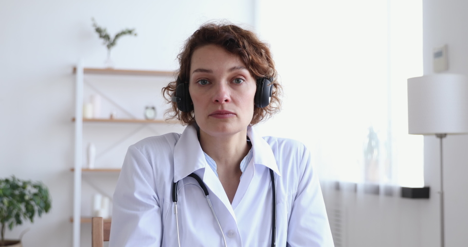 Female doctor wears headset speaking looking at web cam providing remote medical assistance in virtual chat. Medic worker video calling consulting patient online. Telemedicine concept. Webcam view Royalty-Free Stock Footage #1048920538