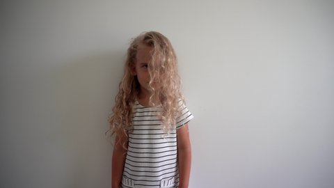 Playful blond girl with wet hairs after bathing pose in front of camera on white wall background. Gimbal motion shot.