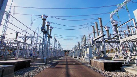motion along powerful electrical transmission substation with equipment and overhead power lines under blue sky on sunny day