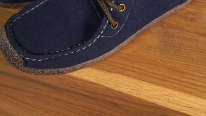 Closeup top view video of leather blue mocassins isolated on brown wooden background.