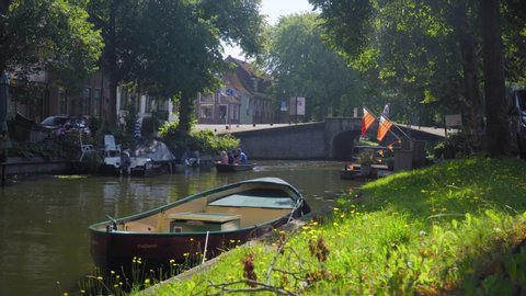 Enkhuizen, The Netherlands - August 24, 2019 - Stationary Shot Of People Sitting In A Small Boat With Lots Of Grass, Trees And Other Boats On A Sunny Day.
