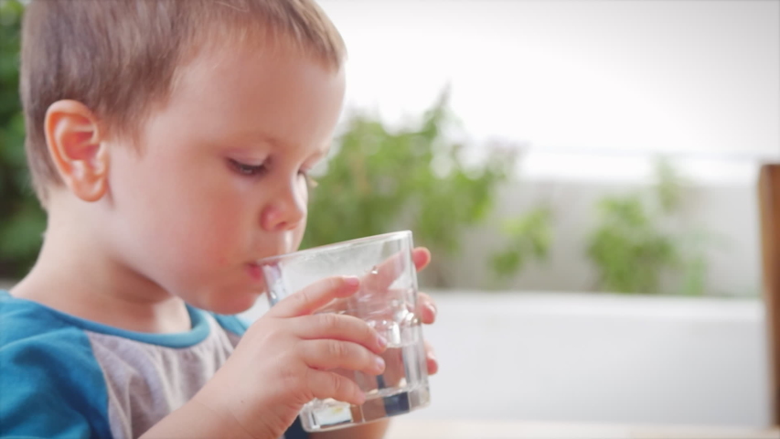 Cute baby boy drinking a glass of water in a cafe. Slow motion little boy drinking water. Close-up. The child is drinking a cup of water. | Shutterstock HD Video #1048943773
