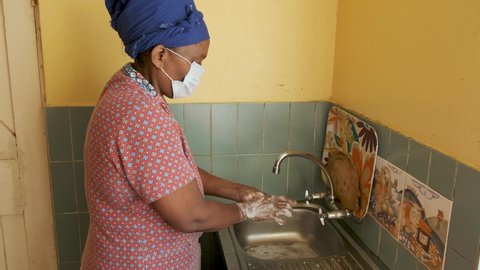 A black South African woman wearing a health mask, washes her hands to prevent Covid-19 infection during Coronavirus pandemic. 