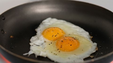 A chef fries an egg, sunny side up, in a small frying pan over industrial gas burning stove with a shallow depth of field.