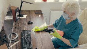 Woman wearing a surgical face mask disinfecting an office workstation cleaning the keyboard of the computer with a sanitizer and cloth to protect against the coronavirus or Corvid-19