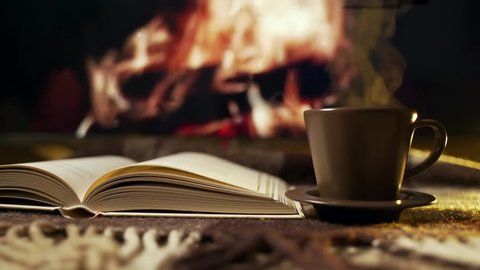 Hygge concept with open book and cup of coffee near burning fireplace. Coffee mood. Background. relax time. 4К 