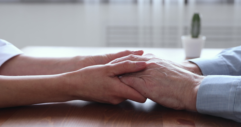 Young woman adult daughter or doctor, caregiver, medical nurse holding old man hands of senior father patient on table. Elderly people health care, support, medicare and comfort concept. Close up view | Shutterstock HD Video #1048970476